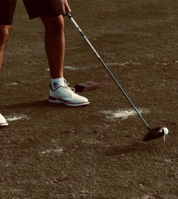 Person playing golf on a grassy field with a club and ball.