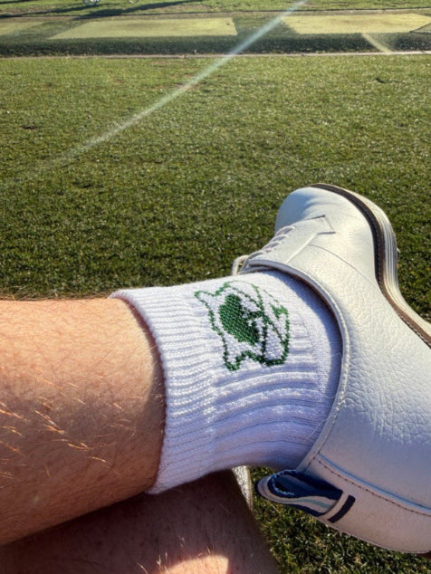 Close-up of a foot wearing a white shoe and green socks with a logo on grass